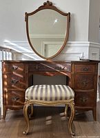 Full frontal view of the wooden vanity table, mirror, and upholstered stool with striped fabric upholstery