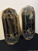 Two prism-shaped Mercana Olaf wall sconces with mirrored backing and gold metal geometric frames, each holding two candle holders.