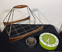 Photo showing all three items: brass/walnut magazine rack with wooden handle, Vecta chrome ashtray with spiral design, round green and white Caravelle wall clock.