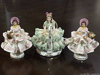 Front view of all three figurines showing two girls with baskets in pink and one girl playing harp in green lace dress.