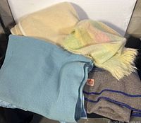 Photo showing all four blankets folded and stacked, featuring the pastel mohair blanket with fringe, blue blanket, cream blanket and Eaton beige blanket.