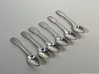 Six sterling silver teaspoons arranged in a row showing shape, size, and monogram on handle ends.