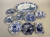 Overview of all 8 Delft pottery pieces showing varied shapes and detailed scenes in blue and white on ceramic.