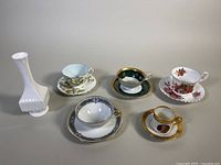 Photo showing five demitasse teacups and saucers of varied designs and one white square toss vase.