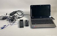 Dell Inspiron P07T laptop opened with power cord, charger, and two removable accessories on white surface.