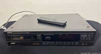 Front view of the Denon compact disc player with remote on top, showing general condition and full unit dimensions.