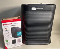 Black Honeywell HPA300CV1 air purifier with box of pre-filters beside it on the floor.