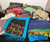 Large assortment of scarves piled on a surface showing multiple colors and patterns including floral, paisley, and stripes.