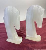Pair of hand carved white onyx horse head bookends photographed together on a maroon cloth background.
