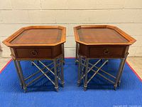 Pair of vintage Hekman wooden side tables viewed from front on a blue protective mat against a beige wall showing overall shape and design.