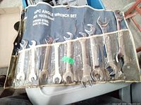 Photo of all 14 angle wrenches in blue fabric pouch, showing sizes labeled 10 to 32 mm, used condition with some rust.