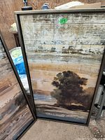 Framed landscape painting showing tree against layered background of earth tones.