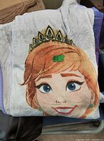 Folded blanket showing the printed face of a female Frozen character wearing a crown.