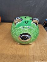Front view of green ceramic piggy bank with chrome accents and coin slot on top