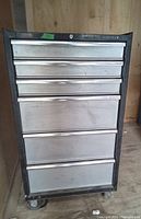 Front view of black Husky tool chest showing six stainless steel front drawers and four swivel caster wheels