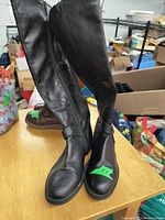 Photo of black ladies winter boots size 6 with inside zippers shown standing upright on a wooden surface, visible strap detail on ankle area, boots appear used with some creasing on material.