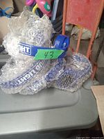 Four blue Bud Light branded headphones partially wrapped in bubble wrap, arranged on a table with a green label marked 43.