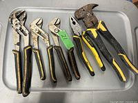 Seven hand tools on a metal tray, including various pliers of differing sizes and a hammer with a worn head.
