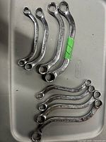 Photo showing nine chrome SAE, box-end wrenches, arranged on a surface. Sizes are visible on some wrenches.