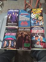 Photo showing six Star Trek paperback books with titles and authors, some featuring characters from Star Trek series and one crossover with X-Men.