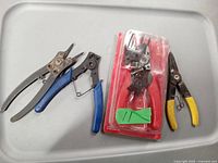 Four hand tools including pliers, cutters, and a new crimping tool in blister pack, all on a white surface.
