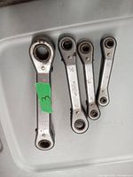 Four offset ratchet wrenches of varying sizes laid out on a plastic surface, showing metal finish and size markings.