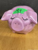 Front view of the pink ceramic piggy bank showing the closed eyes with painted eyelashes and the overall rounded pig shape.