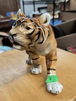 Front side view of the porcelain tiger figurine showing the detailed face, ears, and front legs with a green tag on one paw.