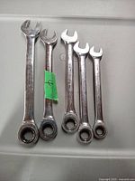 Top view of five metal ratcheting wrenches laid out on a grey tray, showing their polished surfaces and different sizes.
