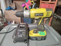 Photo of Ryobi 18 Volt cordless drill with battery and charger on table, showing brand label and condition
