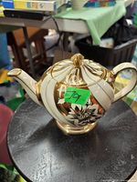 Cream and gold medium size tea pot with floral pattern on black surface