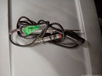Two used electrical test lights laid on a plastic surface. Both have metal probes, wired handles, and insulated black cables, tangled together.