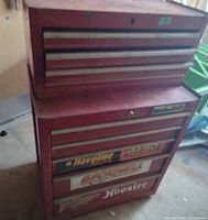 Photo of red two-part metal tool box with multiple drawers and automotive brand stickers, missing wheels.