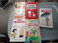 Four vintage small books on carpet including three Peanuts comic collections and one Mad magazine issue.