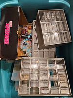 Photo showing jewelry supplies and storage organizers with small clear drawers filled with beads and jewelry making components in a large container.