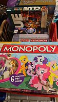 Photo showing Monopoly My Little Pony edition, Monopoly Dead, Clue, partially visible other board games stacked in box