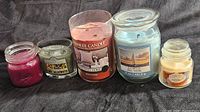Five assorted scented candles displayed from smallest to large, various colors and brands including Yankee Candle