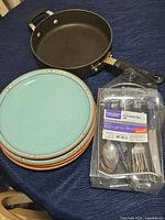 Frying pan with handle, stack of turquoise plates, packaged flatware set