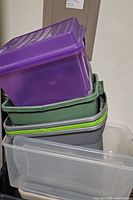 Stack of six assorted plastic storage bins with lids in various colors: purple, green, gray, and clear.