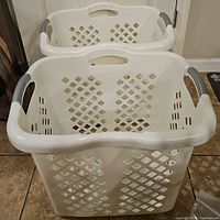 Front and top view of two white plastic laundry hampers stacked inside each other on tile floor.