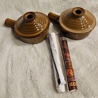 Pair of brown glazed stoneware microwavable cookers with lids and side handles shown with packaging paper.