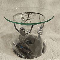 Black metal skeleton-themed candle warmer wrapped in plastic, with round glass plate top