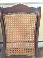 Close view of the cane work on the upper backrest and wooden frame showing wear and wood grain.