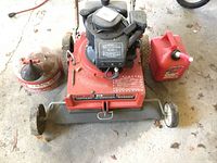 Top down view of a Craftsman red metal lawn vacuum shredder bagger with a 148 CC engine and two gasoline dispensers beside it on the floor.
