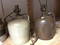 Photo of two ceramic crock urn lamps, one beige and one brown, showing lamps with electrical fittings and a small chip on darker lamp.