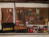 Wide view of lot showing Dewalt drill case, hand saws, hammer, paint cans, and other tools on pegboard and shelf