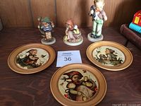 View of the three Hummel figurines and three decorative wooden plates placed on wooden surface showing overall condition and artwork detail.