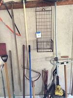 Wide view showing hanging sledge hammer, axe, rakes, broom, shovels, and weed trimmer.
