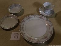 Dinner plates, bread and butter plates, and a cup with saucer showing floral pattern and silver rim.