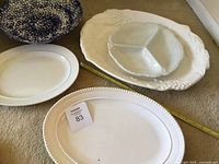 Set showing three white ceramic platters of different sizes and a blue and white salad bowl on floor with measuring tape for scale.